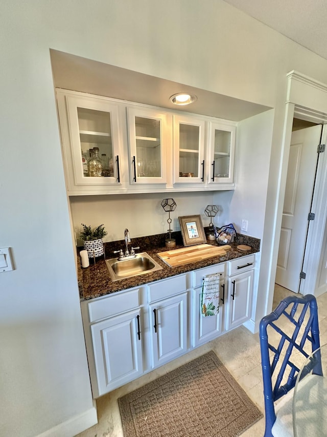 bar with dark stone countertops, white cabinetry, and sink