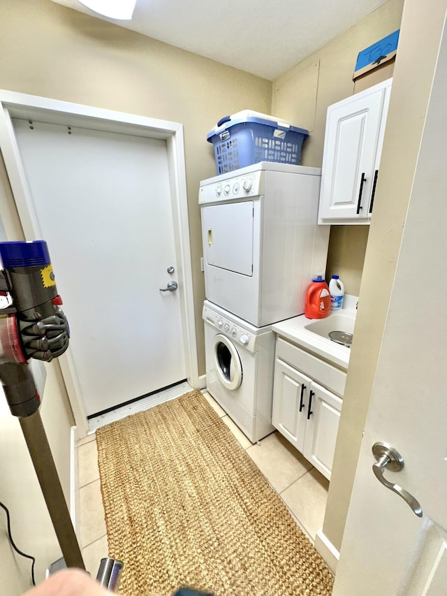 laundry area with cabinets, light tile patterned floors, sink, and stacked washer and clothes dryer