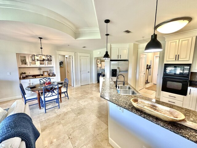 kitchen featuring sink, hanging light fixtures, a raised ceiling, dark stone counters, and black appliances