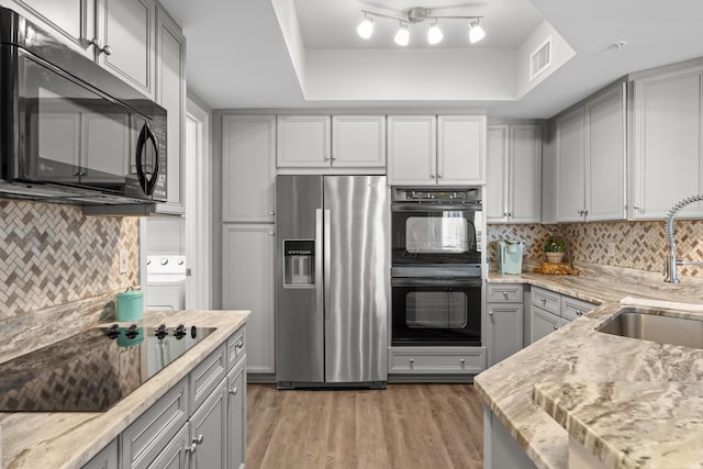 kitchen with black appliances, a raised ceiling, sink, gray cabinets, and light hardwood / wood-style floors