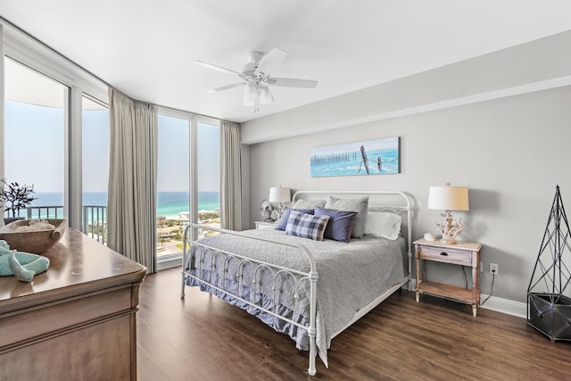 bedroom with access to exterior, ceiling fan, dark wood-type flooring, expansive windows, and a water view