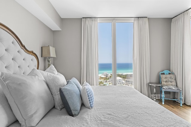 bedroom with a water view, wood-type flooring, and a view of the beach