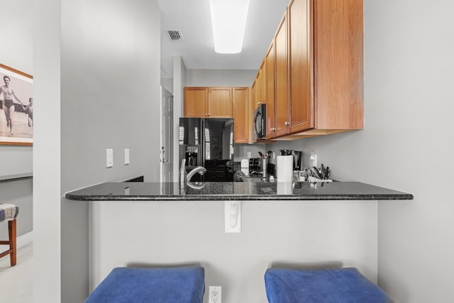 kitchen featuring a breakfast bar, kitchen peninsula, dark stone counters, and black appliances