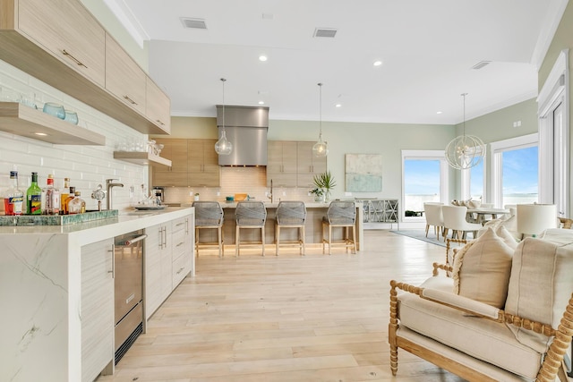 kitchen with backsplash, light brown cabinetry, hanging light fixtures, and light hardwood / wood-style floors