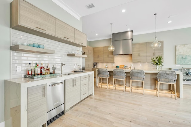 kitchen with light brown cabinets, backsplash, wall chimney range hood, sink, and decorative light fixtures