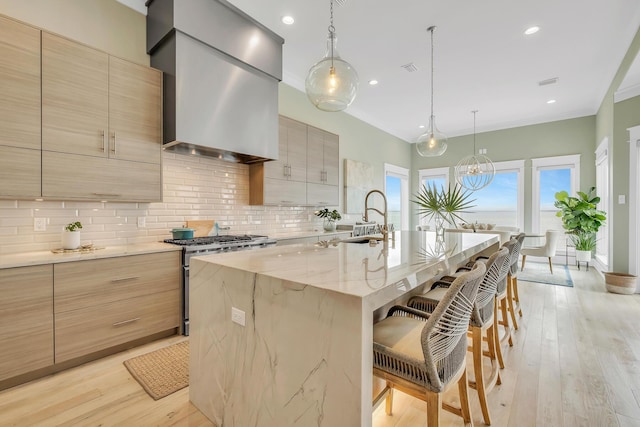 kitchen with a kitchen breakfast bar, wall chimney exhaust hood, stainless steel range, a kitchen island with sink, and sink