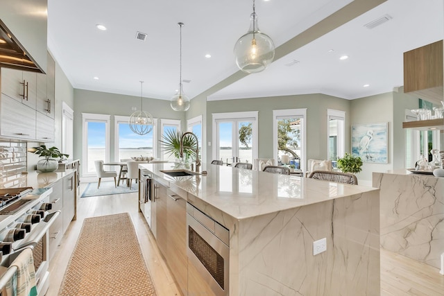 kitchen featuring stainless steel microwave, a large island with sink, decorative light fixtures, gas stove, and light stone counters