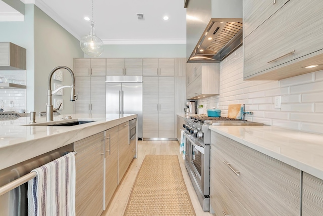 kitchen with light brown cabinetry, light stone counters, wall chimney exhaust hood, high end appliances, and sink