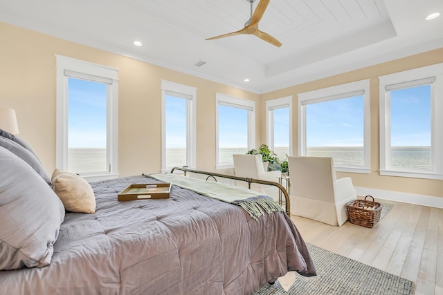 bedroom featuring a raised ceiling, ceiling fan, and a water view