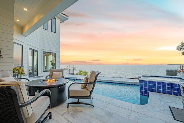 pool at dusk with an in ground hot tub, a water view, a fire pit, and a patio area