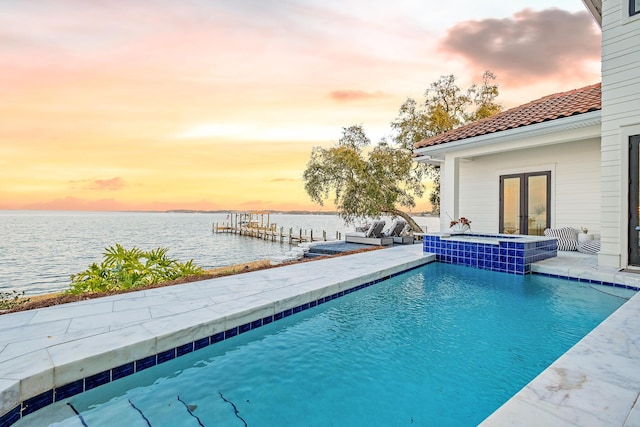 pool at dusk featuring an in ground hot tub, french doors, and a water view