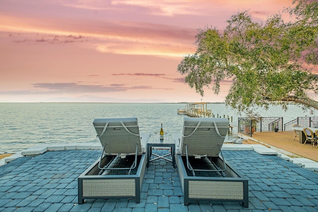 patio terrace at dusk featuring a boat dock and a water view