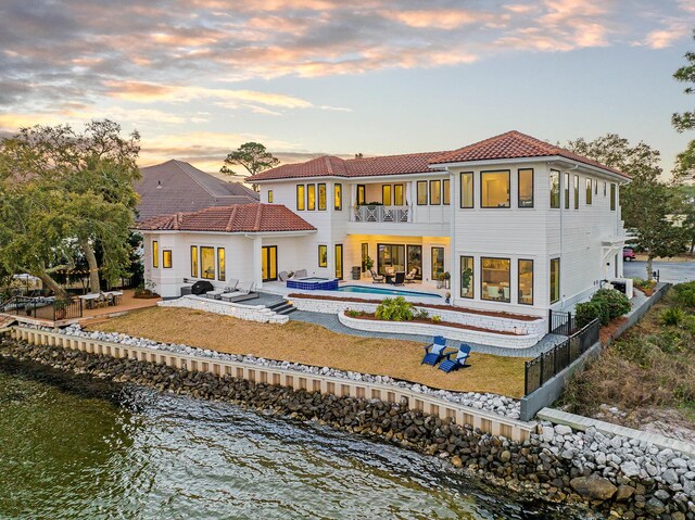 back house at dusk featuring an outdoor living space, a patio, a water view, and a balcony