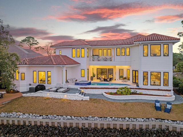 back house at dusk with a swimming pool with hot tub, a yard, a balcony, and a patio area