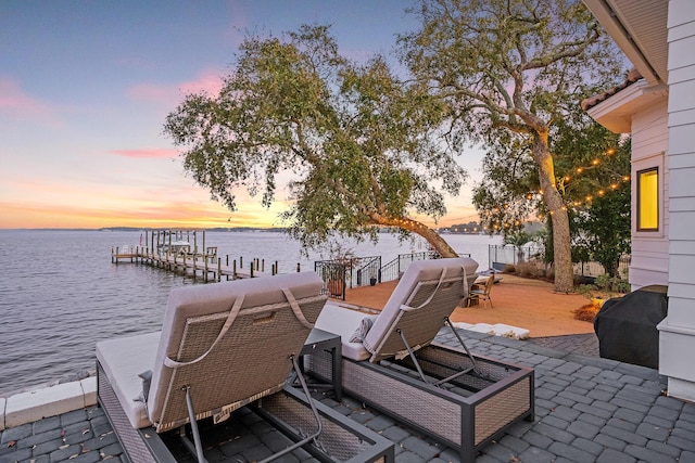 patio terrace at dusk with a grill, a water view, and a dock