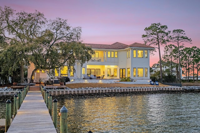 back house at dusk featuring a patio, a water view, and a balcony