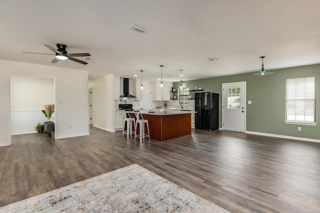 kitchen featuring decorative light fixtures, a breakfast bar area, a center island, black fridge with ice dispenser, and wall chimney range hood