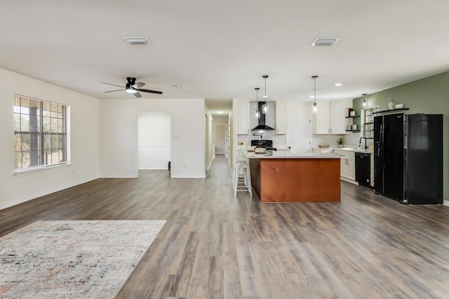 kitchen featuring wall chimney exhaust hood, white cabinetry, hanging light fixtures, a kitchen island, and black appliances