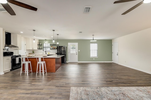 kitchen featuring white cabinetry, a kitchen breakfast bar, a center island, black appliances, and wall chimney exhaust hood