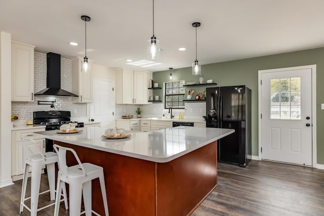 kitchen with a spacious island, wall chimney range hood, white cabinets, and black appliances