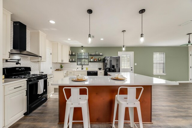 kitchen featuring wall chimney range hood, a breakfast bar area, black appliances, white cabinets, and a kitchen island