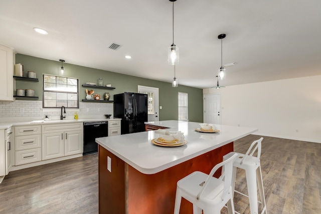 kitchen featuring sink, a breakfast bar area, white cabinetry, a center island, and black appliances