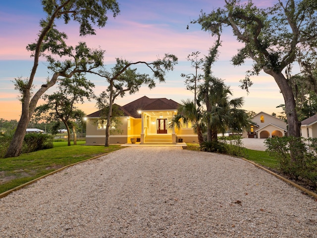 view of front of property featuring gravel driveway, a lawn, and stucco siding