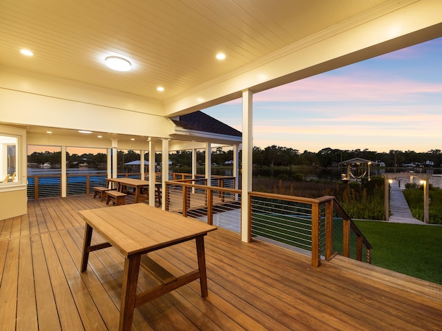 deck at dusk featuring a lawn and a dock