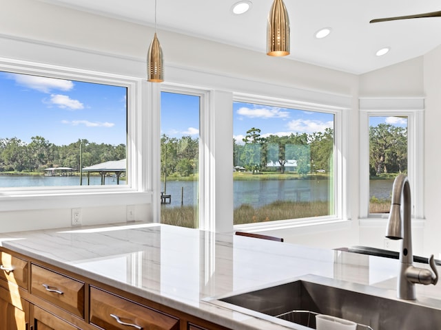 kitchen with light stone counters, a water view, a sink, and brown cabinets