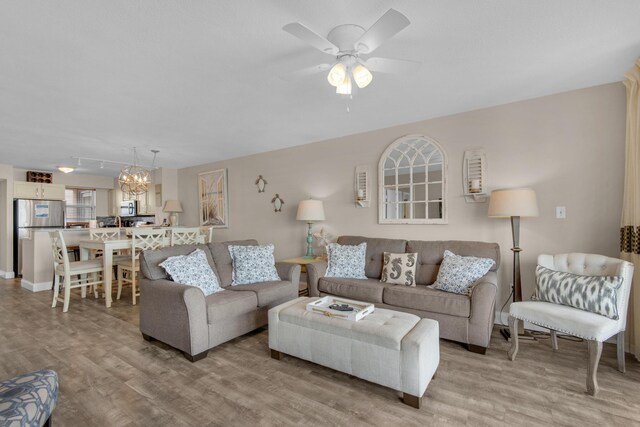 living room featuring ceiling fan with notable chandelier and light wood-type flooring