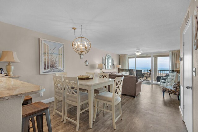 dining space featuring ceiling fan with notable chandelier, hardwood / wood-style flooring, a water view, and a wall of windows