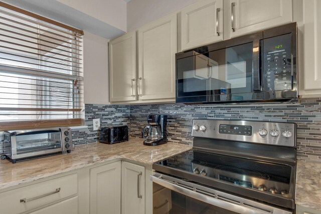 kitchen featuring decorative backsplash, light stone countertops, white cabinetry, and stainless steel range with electric stovetop