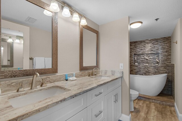 bathroom with toilet, a textured ceiling, hardwood / wood-style flooring, vanity, and a tub