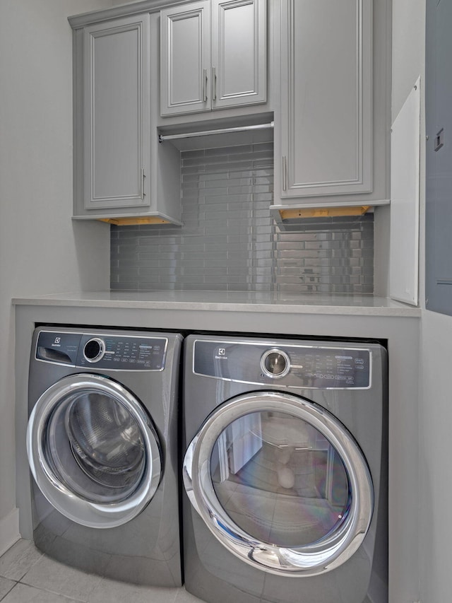 laundry room with washing machine and clothes dryer, light tile patterned floors, and cabinets