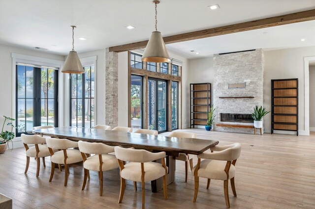 dining area featuring beam ceiling, light hardwood / wood-style flooring, and a brick fireplace