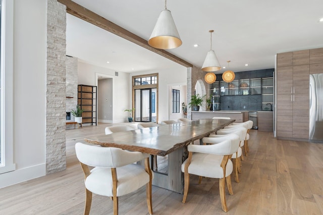 dining room with beamed ceiling, a stone fireplace, and light hardwood / wood-style flooring