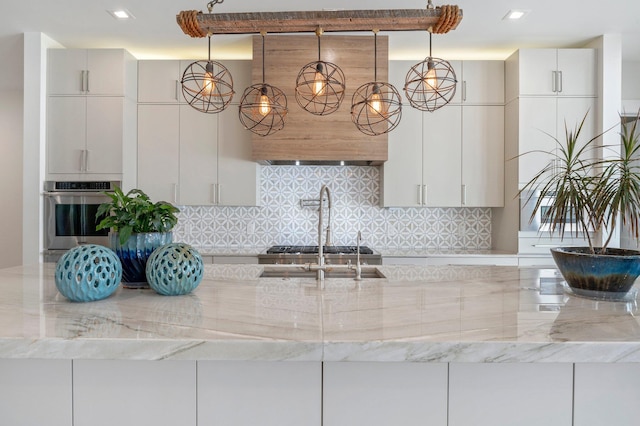 kitchen with stainless steel oven, white cabinets, range hood, tasteful backsplash, and light stone counters