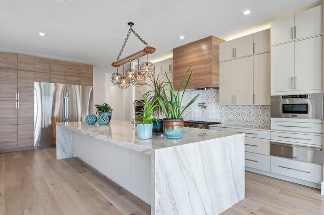 kitchen with ventilation hood, hanging light fixtures, decorative backsplash, a large island, and stainless steel appliances