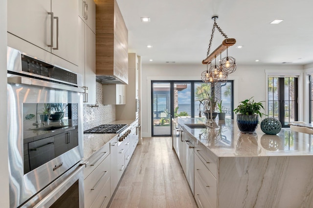 kitchen featuring decorative backsplash, a center island with sink, white cabinetry, and sink