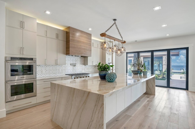 kitchen with a center island, stainless steel double oven, light stone counters, decorative light fixtures, and custom range hood