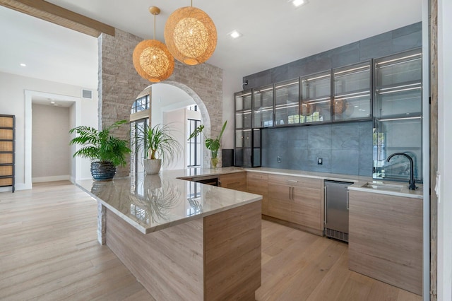 kitchen featuring pendant lighting, sink, light stone countertops, light hardwood / wood-style floors, and kitchen peninsula