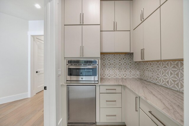 kitchen with stainless steel oven, light stone counters, backsplash, refrigerator, and light wood-type flooring