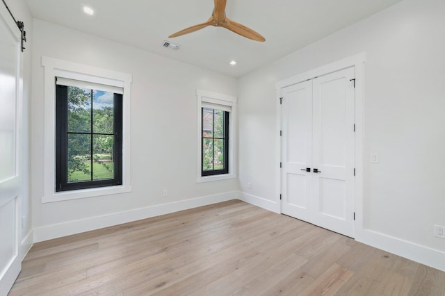 unfurnished bedroom featuring a barn door, a closet, light hardwood / wood-style flooring, and ceiling fan