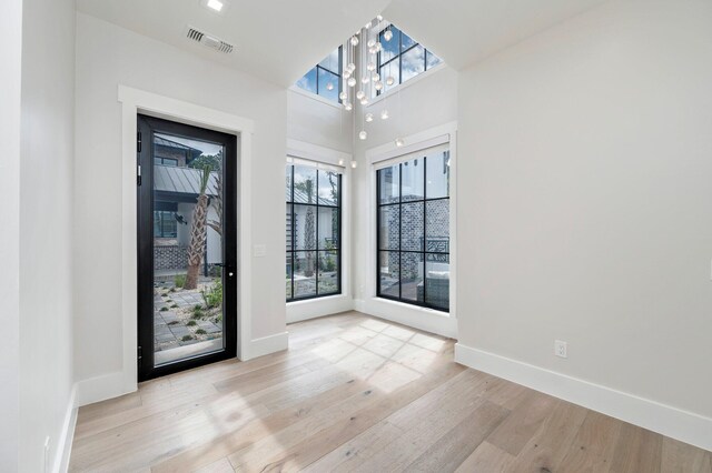 spare room featuring a chandelier, light hardwood / wood-style floors, and a healthy amount of sunlight