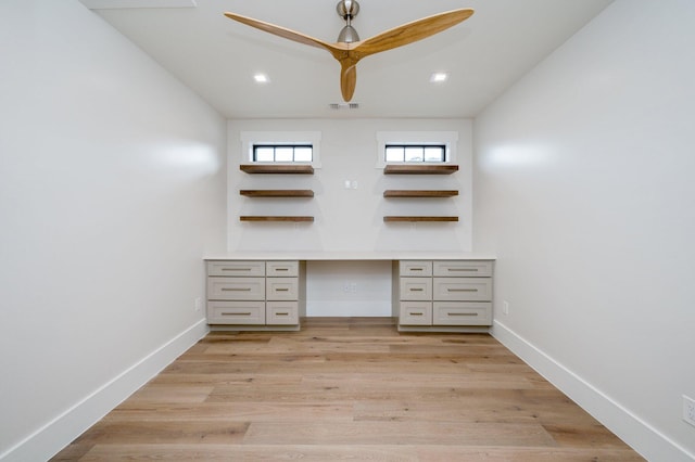 unfurnished office featuring built in desk, light hardwood / wood-style floors, and ceiling fan