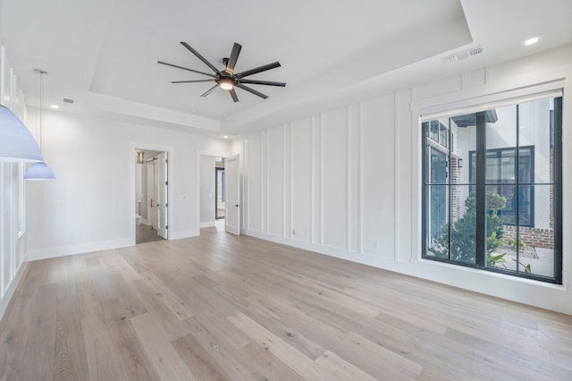 unfurnished living room with a tray ceiling, light hardwood / wood-style flooring, and ceiling fan