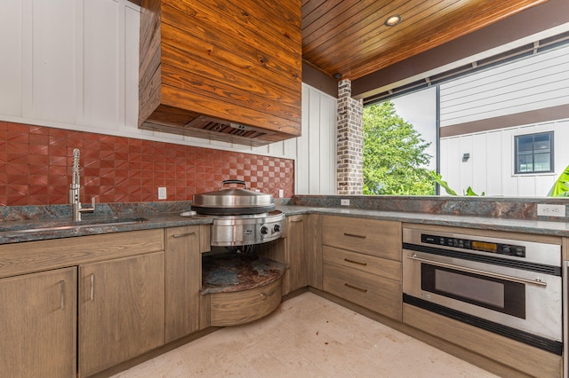 kitchen with sink, stainless steel oven, backsplash, dark stone counters, and wood ceiling