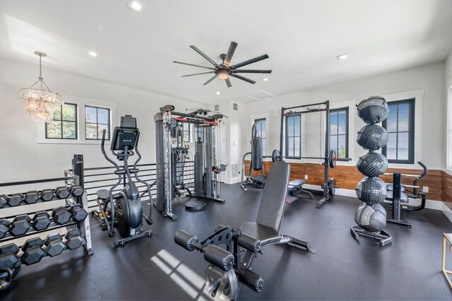 gym featuring ceiling fan with notable chandelier