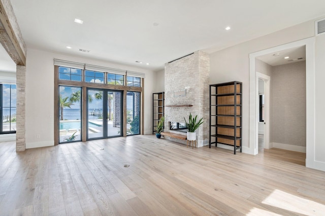 unfurnished living room with plenty of natural light, a stone fireplace, french doors, and light hardwood / wood-style flooring