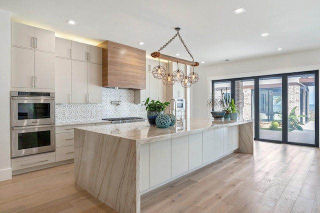 kitchen with a large island, stainless steel appliances, hanging light fixtures, light stone counters, and custom exhaust hood